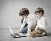 Two little boys sitting with a laptop in a grey room