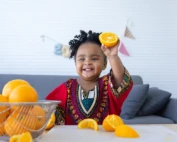 Cute African baby girl showing the halved orange fruit in hand.