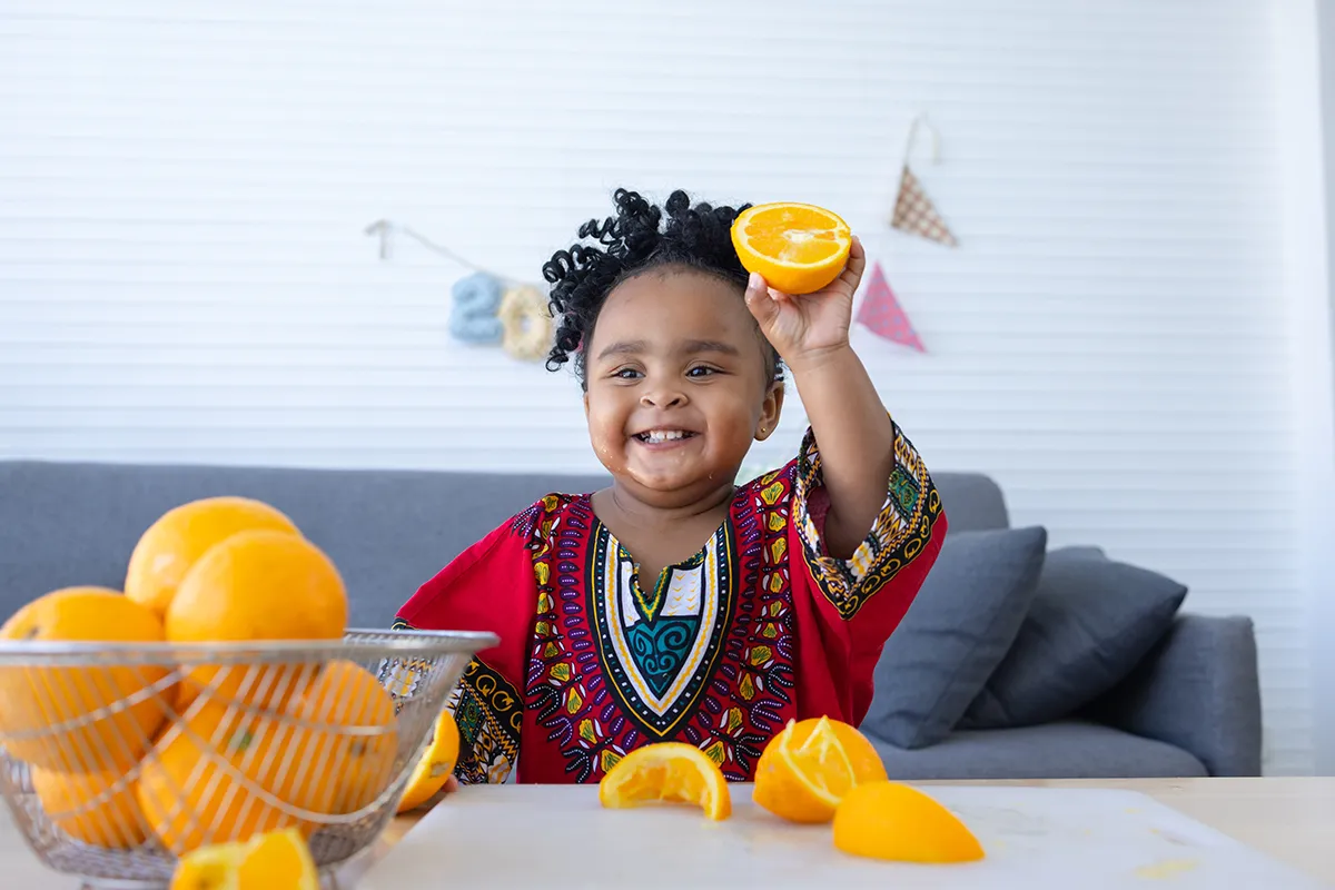 Cute African baby girl showing the halved orange fruit in hand.
