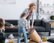 tired mother putting toys in basket while naughty children playing at home | Difficult children