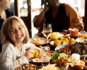 a little girl and her family sitting at a table full of food for Thanksgiving laughing and being merry