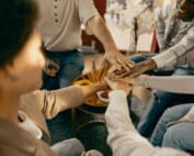 Close up of friends holding hands together while sitting on sofa discussing life's challenges and how they cope on a day to day.