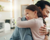 Father and daughter share a warm hug in a bright kitchen, reflecting emotional health, stress relief, and the fulfillment of a child’s emotional need for connection.