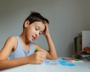 Young boy concentrating while drawing with colored pencils at a desk.