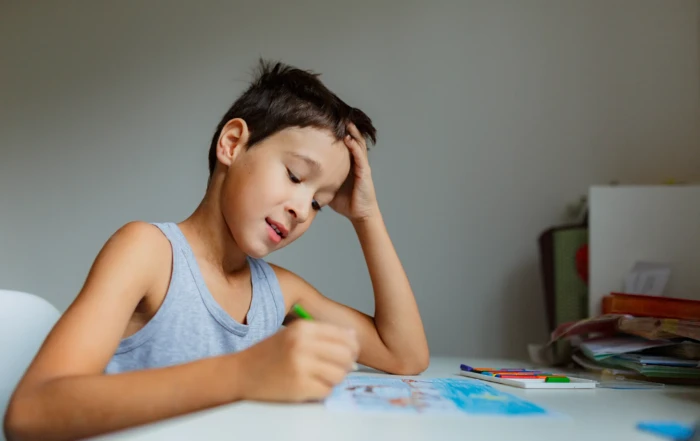Young boy concentrating while drawing with colored pencils at a desk.