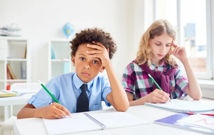 Schoolboy looking frustrated while doing classwork beside a focused schoolgirl.
