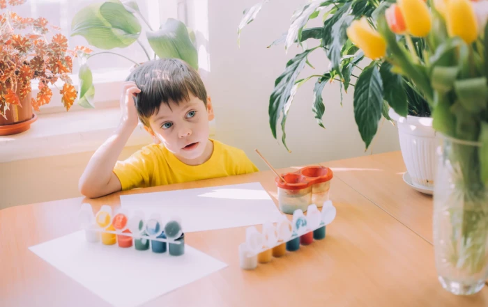 Child sitting at a table looking tired while painting, illustrating signs baby is sick and the importance of visiting a pediatrician in McKinney to check for developmental or health concerns.