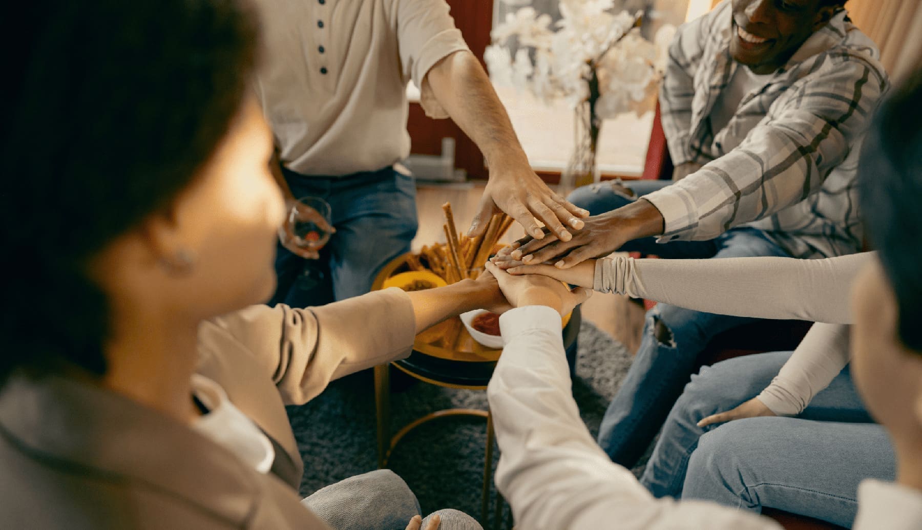 Close up of friends holding hands together while sitting on sofa discussing life's challenges and how they cope on a day to day.