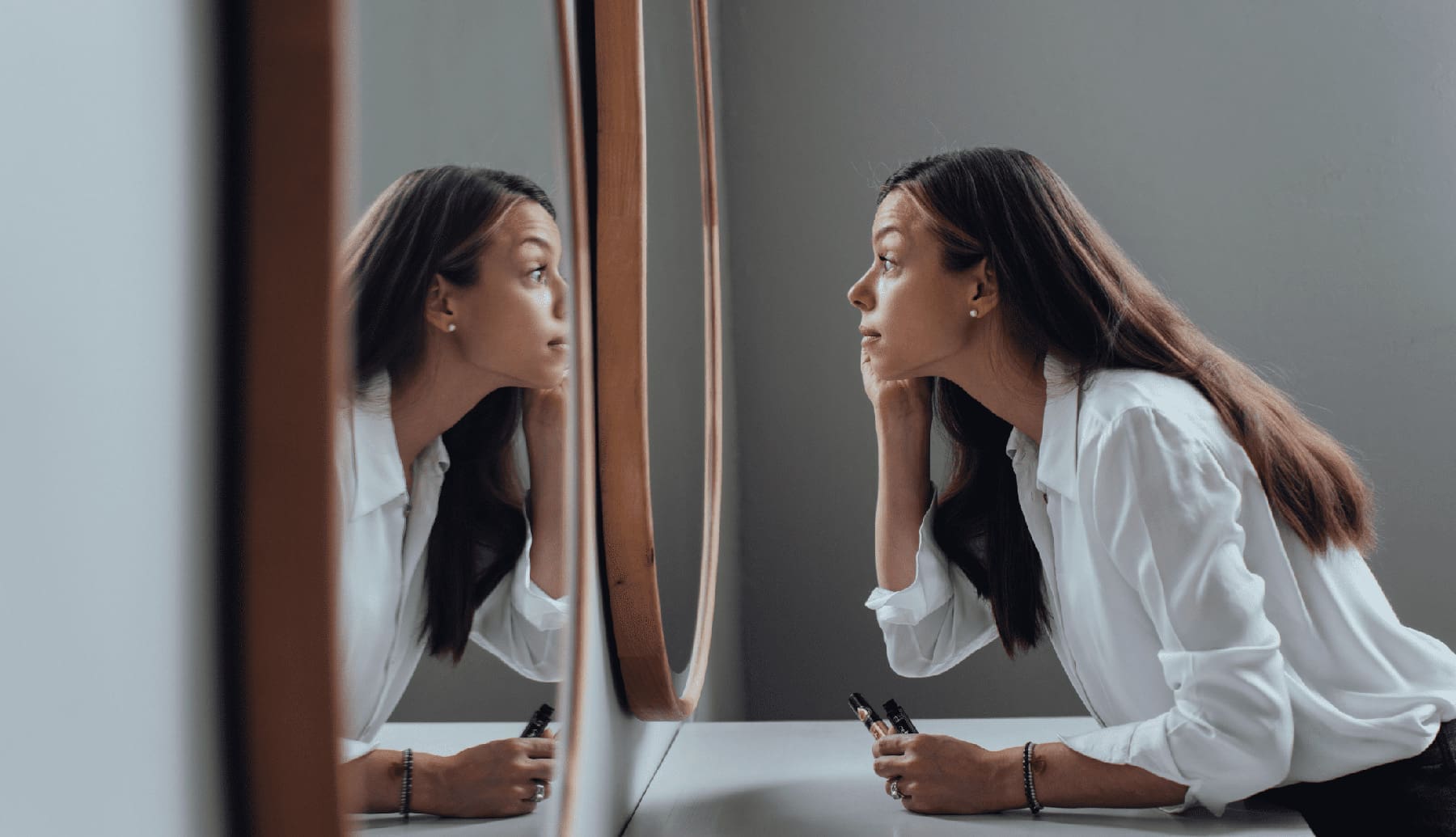 A woman looks into a mirror as she self reflects on her self image and she feels about herself.