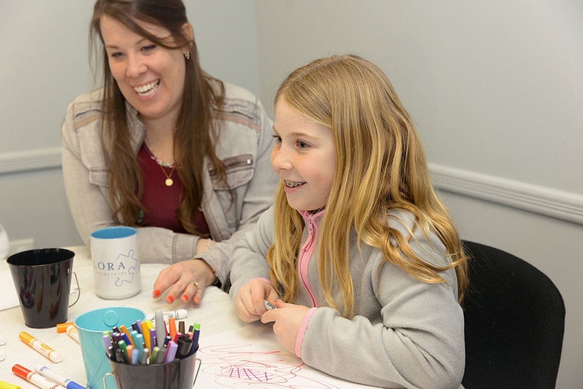 Flora-and-Associates-Kids-0031 A child and a therapist sitting and drawing and smiling and laughing together during art therapy at Flora and Assosiates