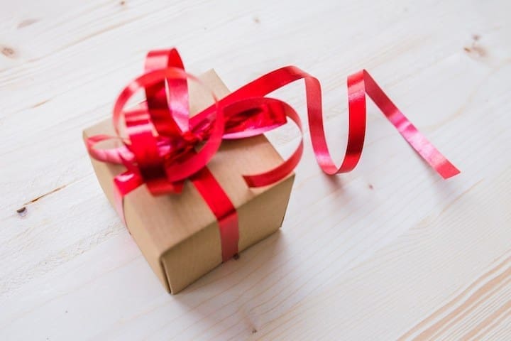 A gift box being wrapped with ribbon.