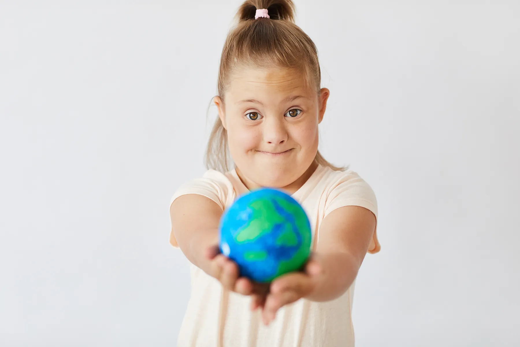 Young girl with Down syndrome smiling and holding a small globe forward, symbolizing inclusion, global awareness, and World Down Syndrome Day.