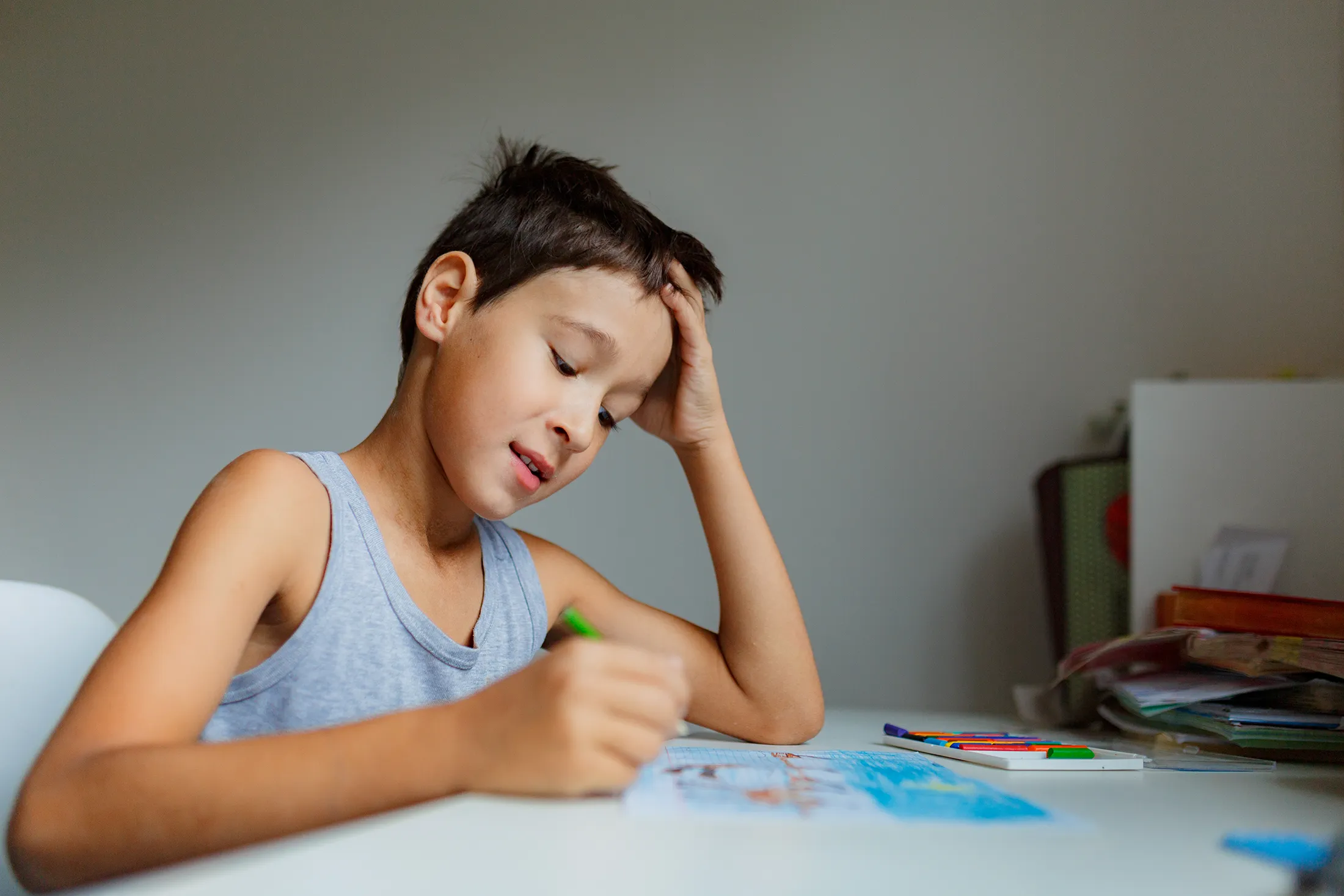 Young boy concentrating while drawing with colored pencils at a desk.