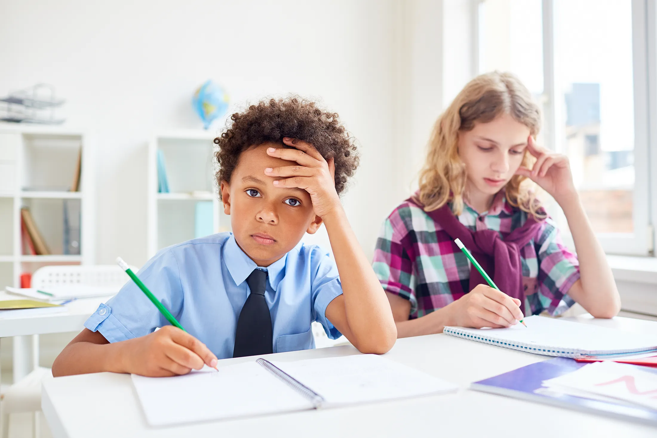 Schoolboy looking frustrated while doing classwork beside a focused schoolgirl.